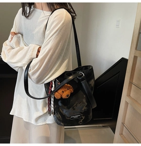 Close-up of black glossy bucket bag featuring a cute brown teddy dog plush pendant