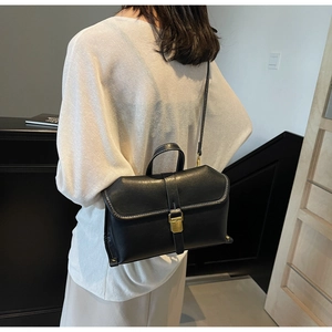 Detail of black matte leather crossbody bag with white stitching and gold metal buckle