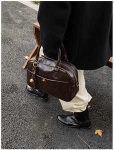 Close-up of a vintage dark brown leather tote bag with a metallic bell pendant detail