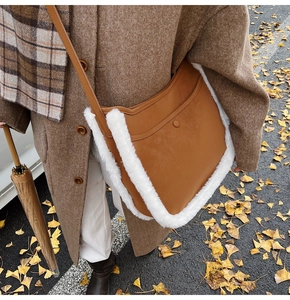 Detail of a brown leather crossbody bag with white faux fur trim on a winter street