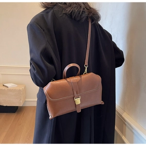 Close-up of retro brown shoulder bag with white stitching and metallic buckle detail