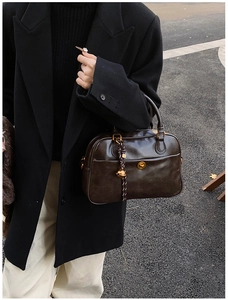 Detail of dark brown leather tote bag with gold hardware and bell charm on a model