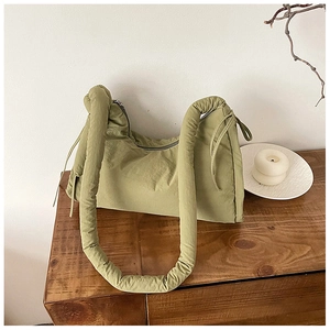 Detail of green puffy nylon bag with chunky padded shoulder strap on a wooden table