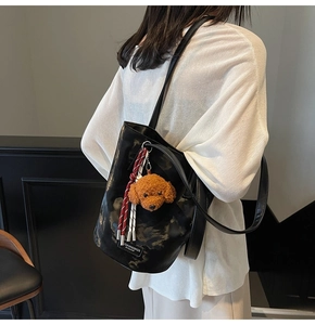 Detail of black bucket bag with marble texture, teddy plush charm and braided cord accent