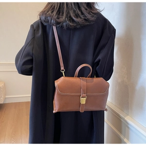 Brown retro leather satchel with golden buckle worn on a black coat by a model