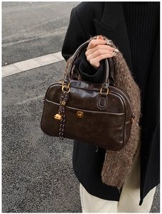 Close-up of retro brown Boston bag with golden twist lock and woven spherical charm
