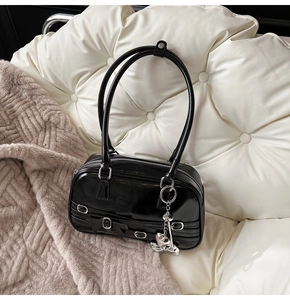 Détail du sac sous le bras noir brillant avec nœud et pendentif cœur argenté