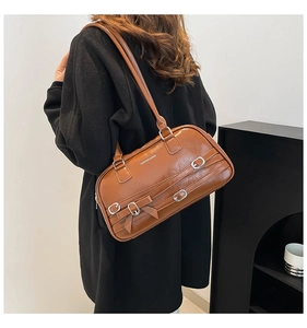 Détail du sac boston en cuir marron avec boucles argentées et nœud porté par le modèle