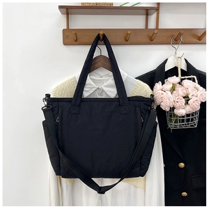 Detailansicht der schwarzen gesteppten Nylon-Einkaufstasche an einer hölzernen Garderobe