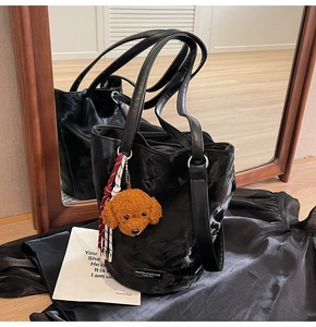 Detail of black PU leather tote with brand label and plush dog charm on a mirror surface