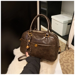 Close-up of vintage dark brown Boston bag with golden buckle and woven bell pendant
