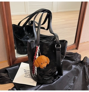 Detail of black pleated faux leather bucket bag with brown teddy bear plush pendant