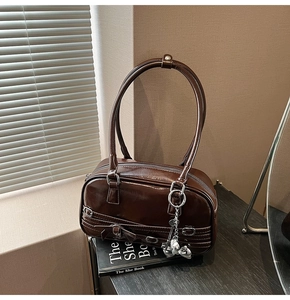 Détail d'un sac baguette marron avec pendentif cœur argenté et bandoulière en cuir PU