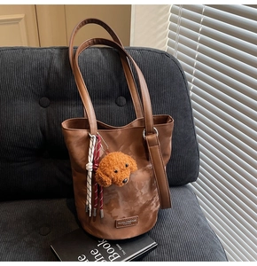 Detail of a dark brown velvet bucket bag featuring a cute teddy bear plush charm and metal logo