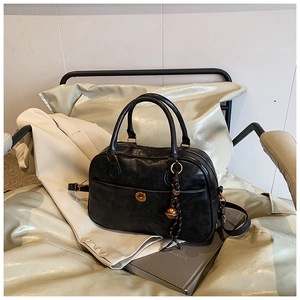 Detail of black vintage satchel with gold lock on leather chair with white blazer