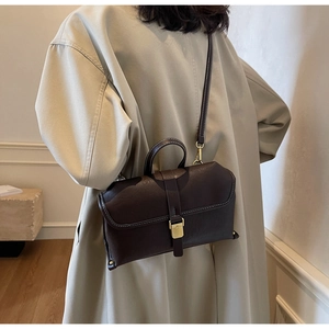Detail of dark brown leather crossbody bag with white stitching and gold buckle