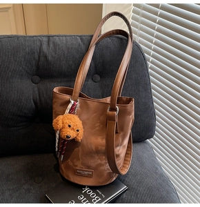 Close-up of brown bucket bag with plush dog charm on a corduroy textured sofa