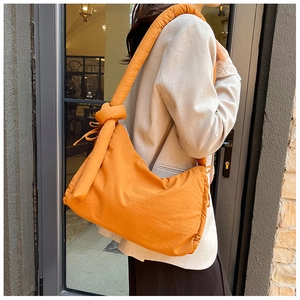 Detail of the oversized orange quilted nylon bag with a stylish knot handle design