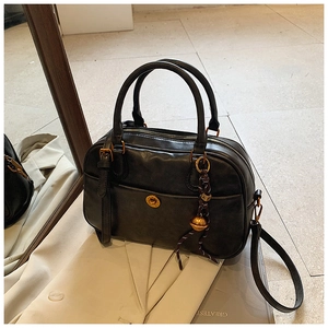 Detail of a vintage black Boston bag with gold buckle on a beige blazer background