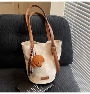 Close-up of cream bucket bag with plush dog charm on a corduroy textured surface