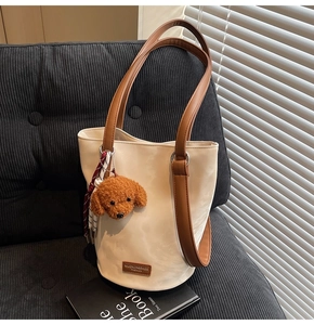 Detail of cream white bucket bag with brown handles and cute teddy bear plush charm
