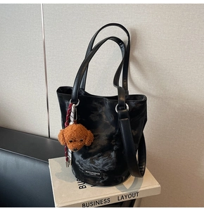Detail of black marble pattern bucket bag with brown teddy bear charm on white book base