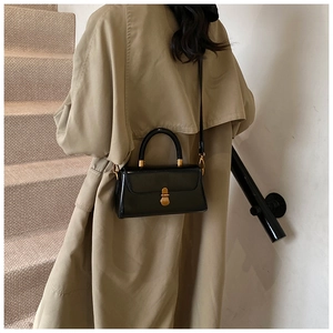 Classic black rectangular shoulder bag with gold clasp shown on a beige trench coat