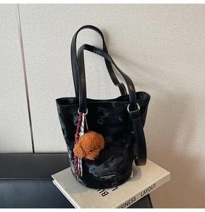 Detail of black marble textured bucket bag with plush dog charm on books