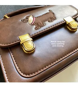 Detail of dachshund embroidery and gold hardware clasp on brown leather handbag