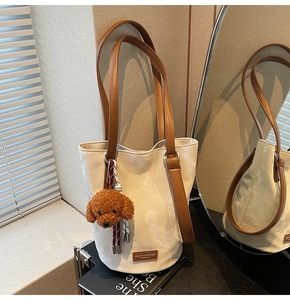 Detail of cream bucket bag with brown leather strap and plush teddy bear charm