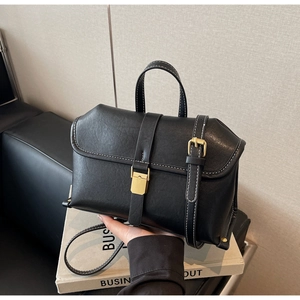 Detail of vintage black leather crossbody bag featuring white stitching and gold hardware buckle