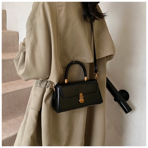 Detail of a black leather square handbag with golden clasp shown on a model's arm