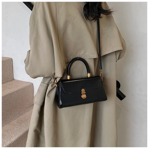 Detail of glossy black patent leather handbag with gold oval lock on a beige trench coat
