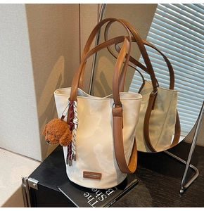 Detail of cream bucket bag showing brown leather straps and plush puppy charm accessory