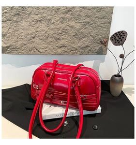 Détail du sac à bandoulière en cuir rouge brillant avec boucles décoratives et nœud en cuir
