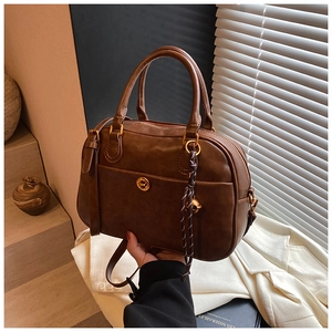 Detailed view of brown retro shoulder bag with golden round lock and woven pendant