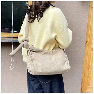 Detail view of beige nylon crossbody bag featuring stylish side ruffles and knotted shoulder strap