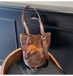 Detail view of brown vintage bucket bag with a cute plush dog pendant on a wooden chair