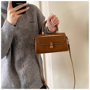 Detail view of a vintage brown leather square handbag with bronze clasp and top handle