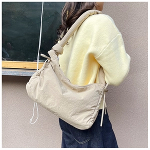 Close-up of beige nylon hobo bag with knotted strap detail on casual street outfit