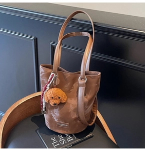 Detail of a brown bucket bag with a plush dog charm and brand logo on synthetic leather
