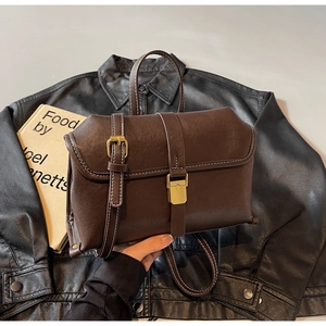 Detail of dark brown vintage leather crossbody bag with white stitching and gold buckles