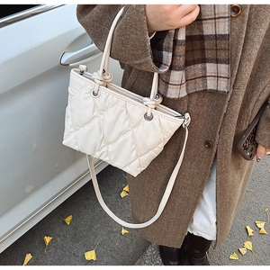 Sac seau matelassé blanc avec poignée nouée et détails argentés sur fond urbain automnal