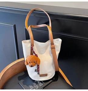 Close-up of white bucket bag featuring a brown leather logo and plush dog charm