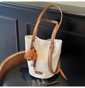 Detail view of a retro cream leather bucket bag with brown handles and a plush dog charm