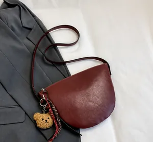 Detail of dark red hobo bucket bag featuring a cute plush bear charm on a grey blazer