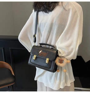 Detail of black leather crossbody bag featuring dachshund embroidery and plush monster charm