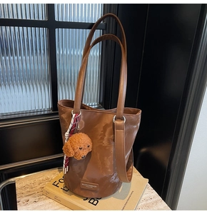 Detail of a brown bucket bag with a plush dog charm and silver metal hardware