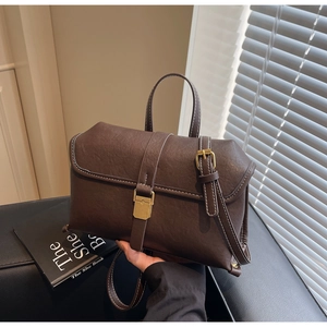 Detail of dark brown retro shoulder bag with white contrast stitching and gold buckle