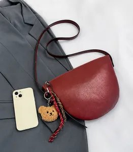 Top view of burgundy leather crescent shoulder bag with plush bear charm and phone size scale